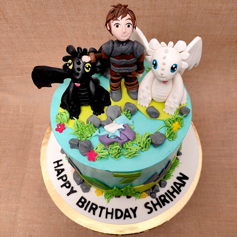 Top view of how to train your dragon cake with toothless and light fury along with hiccup standing on top of dragon theme cake