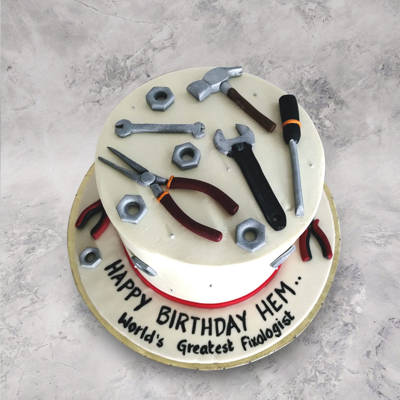 This mechanic theme cake design comes with a minimal white base and displays an array of edible, mechanical tools on top from spanners to pliers, a hammer, a screwdriver and nuts and an edible red ribbon borders the bottom.