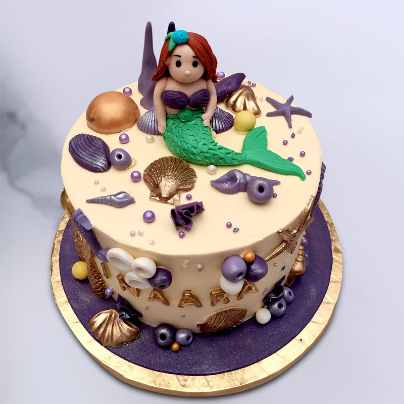 Top view of mermaid theme cake with aerial the cartoon character on top and surrounded by lot of sea creatures for her to play with 