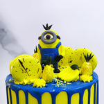 Zoomed front view of Minion cartoon cake with small fondant minion and yellow macarons. 