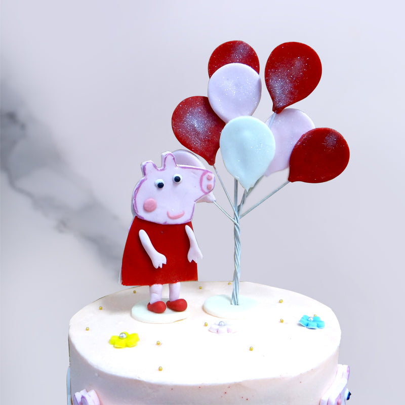 Here's cute little peppa pig standing on top of our 2 tier peppa pig cake design while holding some balloons and cute lovely smile on her face
