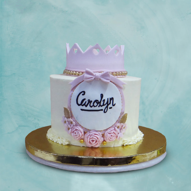 This princess cake has a unique charm to itself holding a pink o top and a circular tiara with name tags on side adds more beauty to this cake with crown