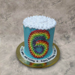 Top view of tall rainbow and clouds cake to showcase the cloud covered top theme and rainbow numbers on side to uplift the joy of your kids 6th birthday celebration