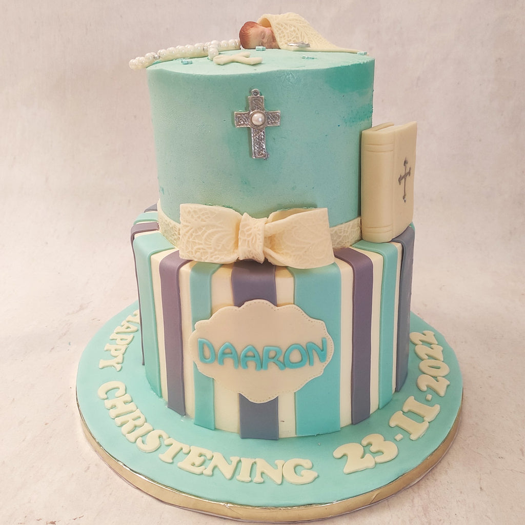 The bottom tier of this Christian themed cake features a vertical purple and blue striped pattern like a wrapped gift with a textured white bow on top.
