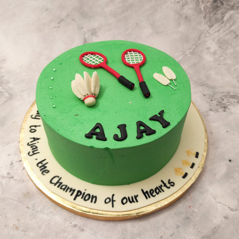 Here's a very simple badminton cake design which entirely comprises of two rackets, two fallen shuttlecock feathers and one shuttlecock laid neatly on a grassy court next to each other all entirely edible and completely customisable to your specifications.