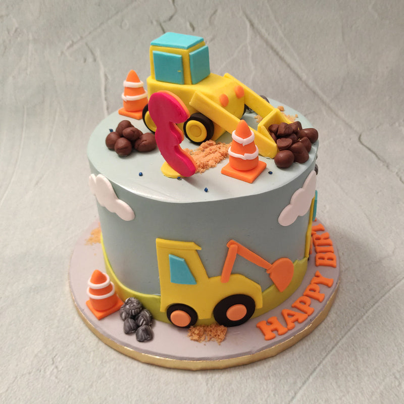 Each of these trucks are carrying chocolate-y pebbles shaped like rocks and marble stones. Cookie crumbs replicate sand on top of this  construction themed cake and the blue base places the cake in the setting of a beautiful, clear skied day with lazy clouds floating by.