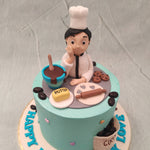 The base of this cooking theme birthday cake for mom / wife  features a sky blue colour palette with a figurine of a chef making dessert. A chocolate bowl, butter, a roller pin, choco chip cookies and cookie dough with heart-shaped cut-outs are present in front of her. 