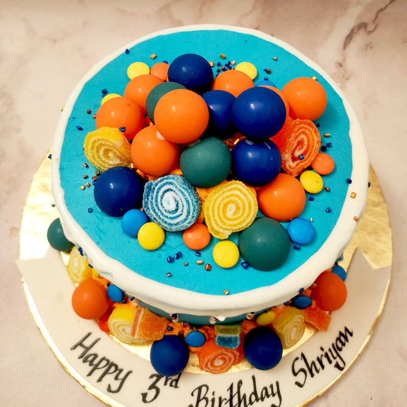 This candy birthday cake for kids features a bright blue base with a creamy frosting forming a wreath around the sides and sliding down in the popular drip design that has gained a lot of traction in recent years.