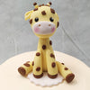 A smooth cream-coloured base with grey, pink and yellow baubles on the base form the body of this giraffe theme cake and the highlight or the showstopper is the cake topper: a miniature, stuffed-toy-like figurine of a giraffe sitting on its haunches. 