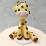 A smooth cream-coloured base with grey, pink and yellow baubles on the base form the body of this giraffe theme cake and the highlight or the showstopper is the cake topper: a miniature, stuffed-toy-like figurine of a giraffe sitting on its haunches. 