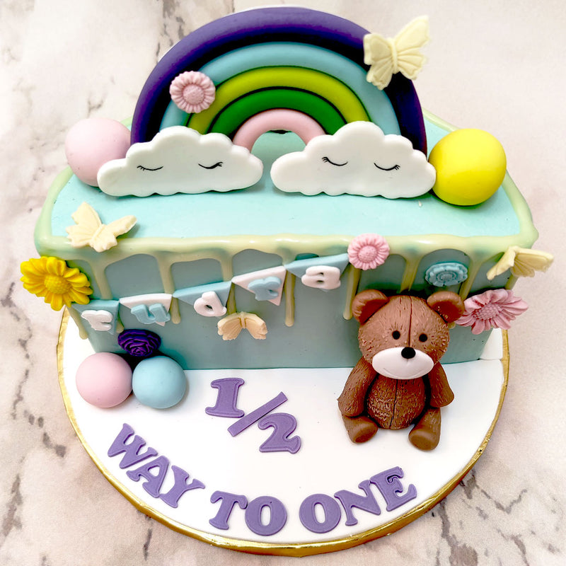 Other edible elements of a nursery on this halfway to 1 cake design are the realistic teddy bear, the sleepy-eyed clouds on top and the pillowy cake-pop balls. However, the most unique aspect of this halfway to one birthday cake for kids is that it comes in the shape of a semi-circle or half-cake to showcase the half year that your little one has completed and is now being celebrated.