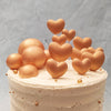 The gold heart cake topper is an array of sugar gold baubles and hearts, arranged to look like miniature helium balloons tied to the heart topper cake. 