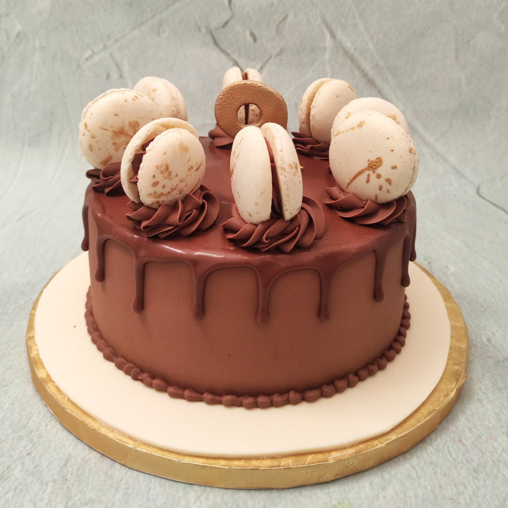 This chocolate macaroon cake features a chocolatey base with creamy chocolate buttercream piping lining the bottom and ornamenting the top with swirls. Embedded into these swirls are white and gold flakes macarons, marble-patterned, crisp on the outside and soft and creamy on the inside. 