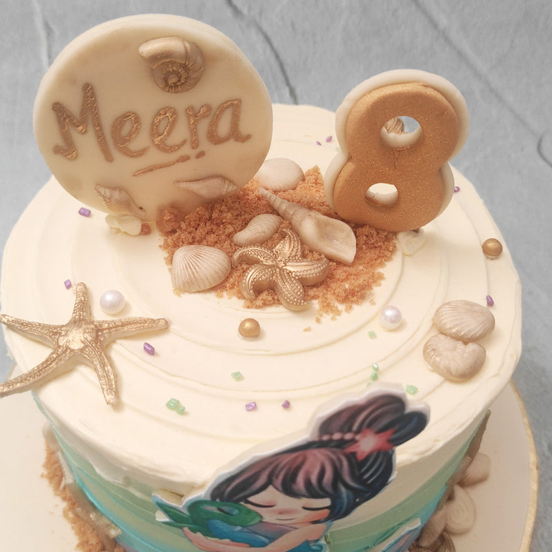 The beach theme of this mermaid birthday cake for kids emerges through the textured buttercream pattern that frosts the base. A wavey cream to green to blue gradient is used to showcase the sea and edible sand, seashells and starfish line the top and bottom of this mermaid theme cake in a way that looks as if they’ve been washed up on shore. 