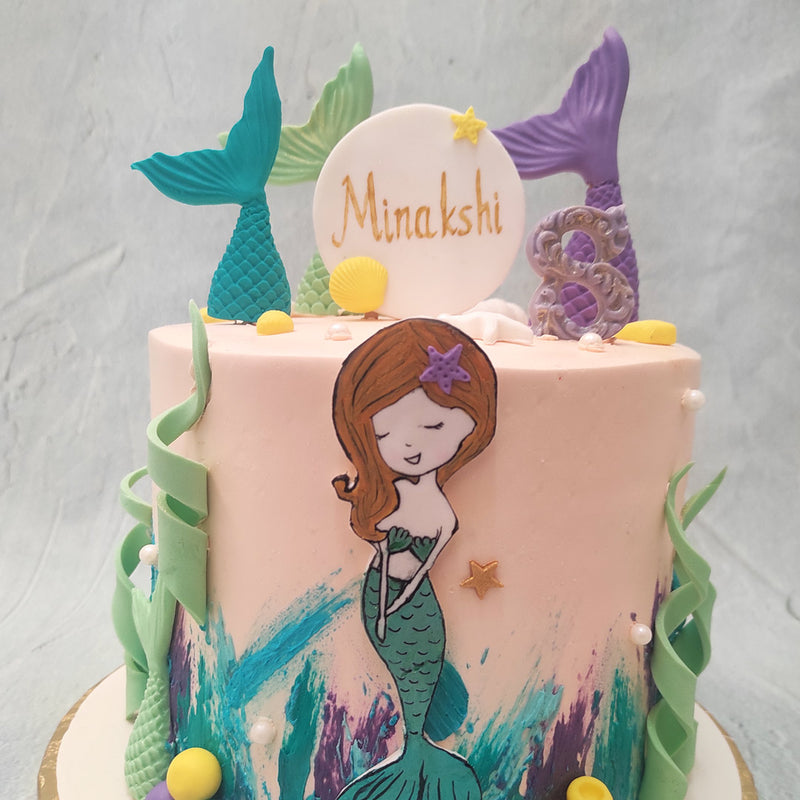 The mermaid tail on cake design also features a poster-like cut-out of a mermaid in her entirety, like a picture from a storybook. Mermaid tails in purple, blue and green are embedded into the top of this mermaid tail cake buttercream dream, making it look like these friendly sea creatures are deep diving straight into the cake as if it is the ocean.
