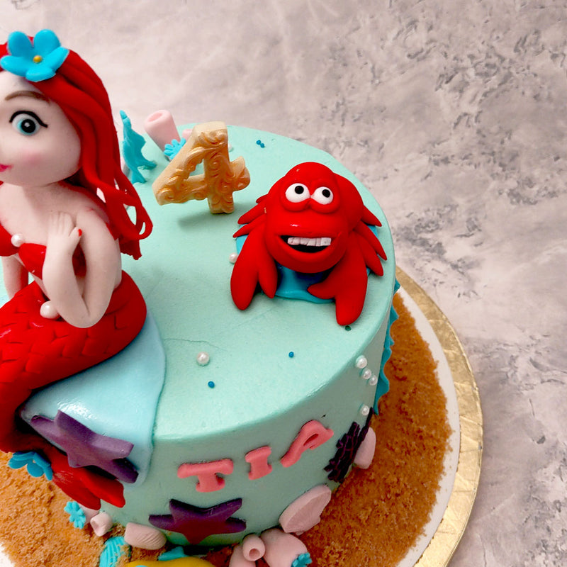 The beautiful princess Ariel with her red hair and a red scaled take, sits daintily on top of this mermaid birthday theme cake, entirely edible and completely customisable to your preferences!