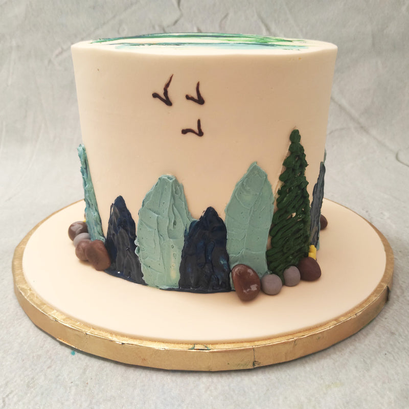 A simplistic and minimalistic design, this mountain birthday cake for him / her is a tribute to mother nature in all her natural beauty and aesthetic. From the edible boulders on the side of this mountain themed birthday cake for her / him to the rolling hills, hand-drawn birds in the sky and pine trees piped on in delicious, velvety frosting, this mountain cake is like something taken straight out of a child’s imagination.