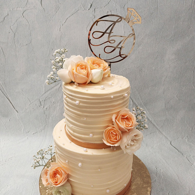 Both tiers of this peach rose cake bear identical designs coating in creamy, textured frosting borrowing a beautiful peach colour palette. Embedded into this velvety frosting on this two tier rose cake are some lustrous, white pearls that add a lavish tone to the design's aesthetic. 