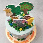 The friendly animals that make up this jungle safari theme cake appear to be playfully hiding and emerging from the flowering bushes, which are piped on with delicious, velvety buttercream both on the top and at the base of this jungle safari birthday cake for kids. These bushes feature colourful flowers and rich, green leaves, similar to the one depicted on the tree placards on the top. 