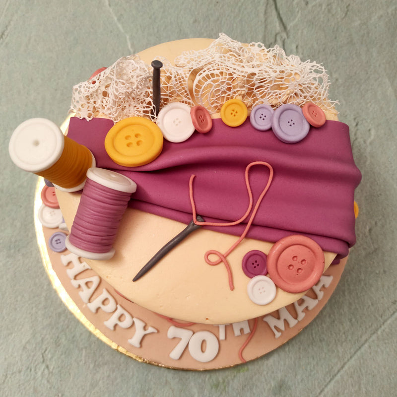This stitching kit cake features a unique design which displays a neutral peach base with an edible lace pattern on the bottom. Life-like cut-cloth, needles, reels of thread and buttons ornament this stitching machine cake design and bring to life the unfinished that seamstresses like to bring to life.