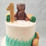 The design of this teddy bear birthday cake for kids follows a simplistic, artistic and minimalistic aesthetic. A clean white finish is present on both tiers, with buttercream smudges representing grass as the base of both tiers. 