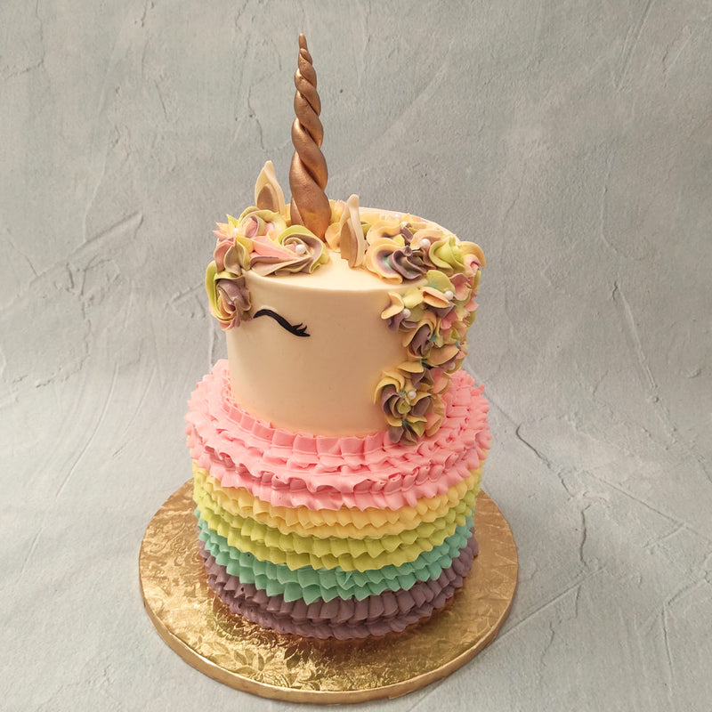 The tall, bottom tier of the two tier unicorn cake displays rainbow ruffles piped on with velvety buttercream frosting which looks like the friendly unicorn is wearing a fluffy skirt. 